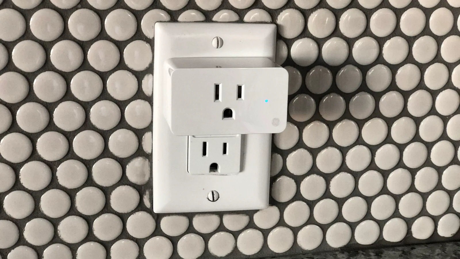 Tomada inteligente branca conectada à parede de uma sala de estar, alimentando um cabo de energia doméstico.